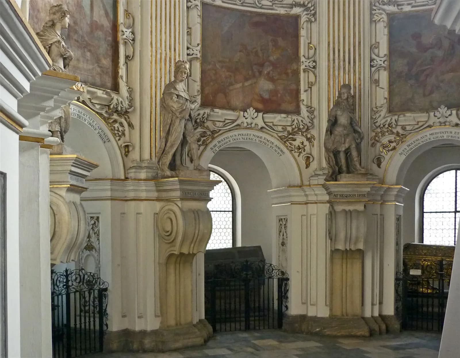 A grand, ornate interior with decorative archways, golden accents, several sculptures of figures, and high-arched windows.